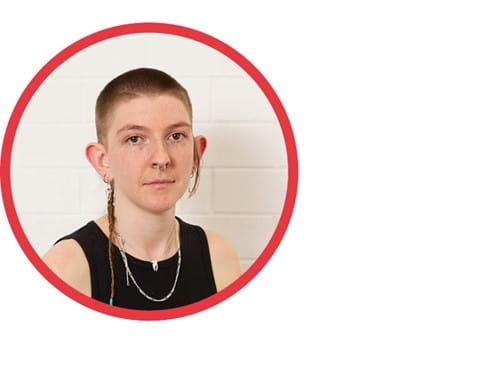 Headshot of Grace Marlow. Grace has pale white skin, brown eyes, and a silver septum nose ring. They are wearing a black tank top and black pants. They have a blonde buzz cut and a thinly braided 'rat's tail', which is draped over their right shoulder. They sit against a white background, looking directly at the camera.